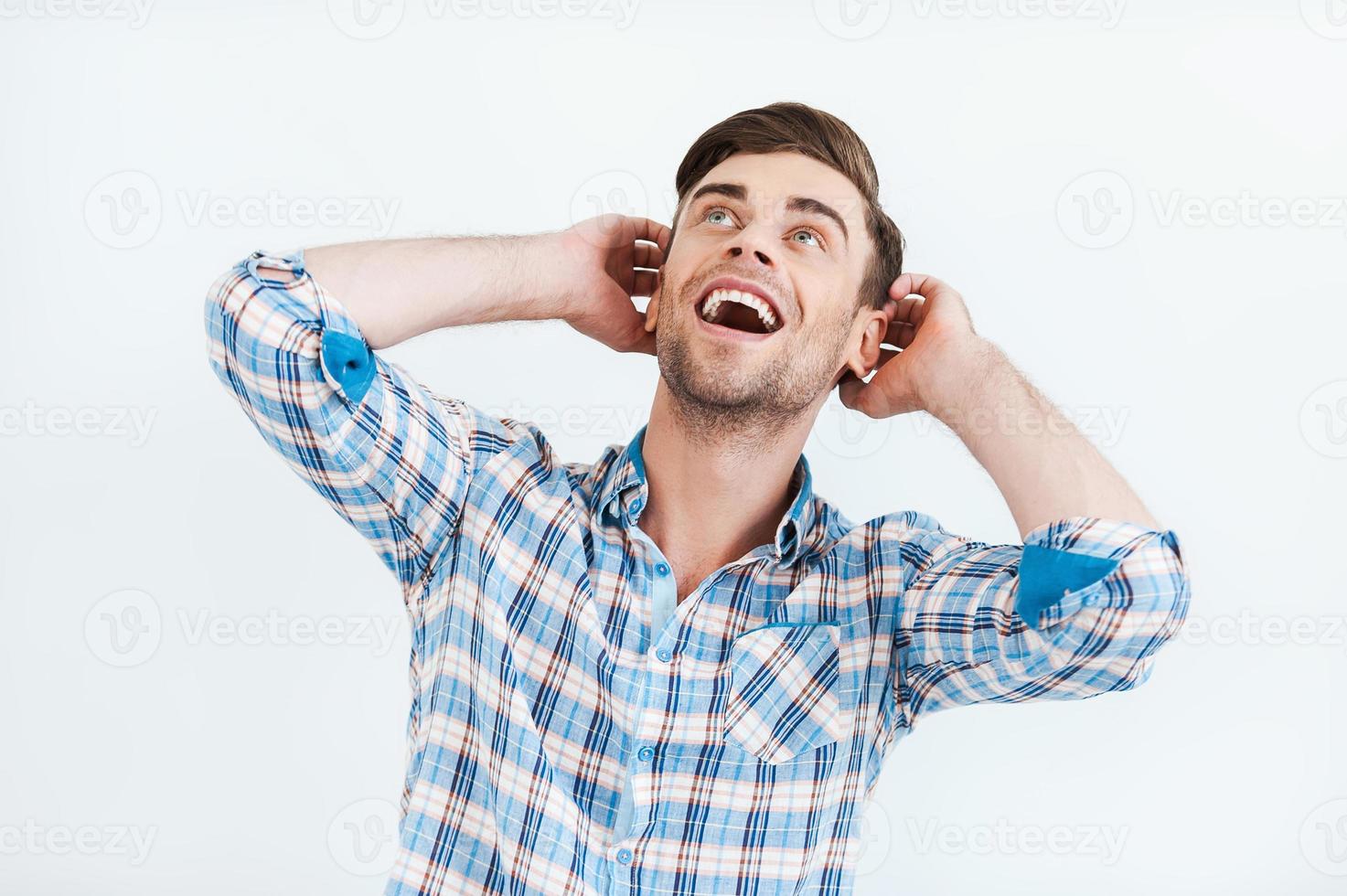 Incredible news. Surprised young man in shirt smiling and looking up while standing against white background photo