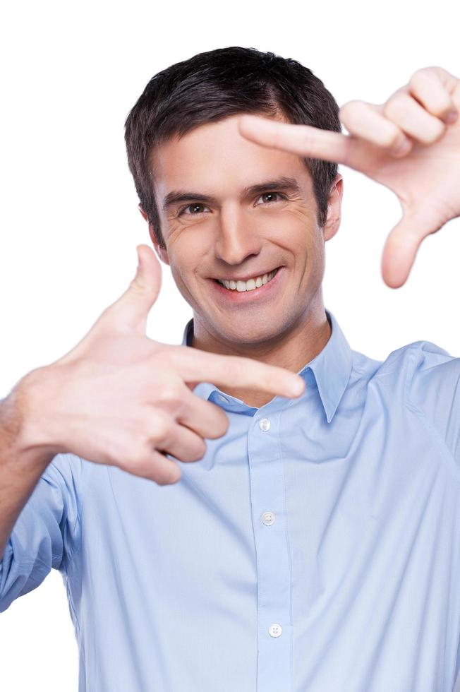 Businessman focusing at you. Portrait of handsome young man in blue shirt looking at camera and focusing at you with fingers while standing isolated on white photo