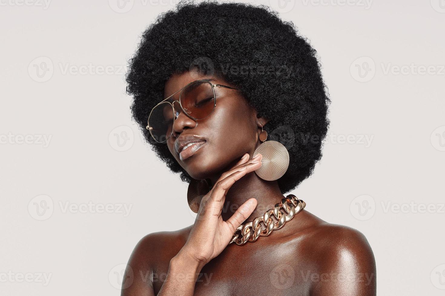 Portrait of beautiful young African woman in golden jewelry keeping eyes closed and touching face photo