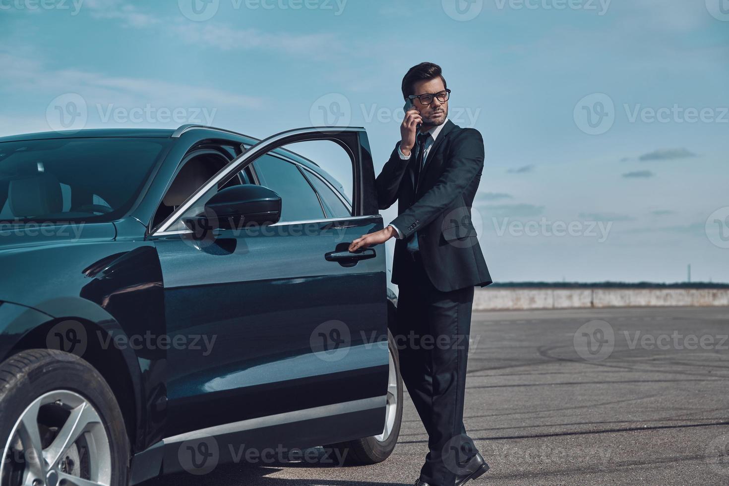 Confident business expert. Full length of handsome young businessman talking on the phone while entering his car outdoors photo