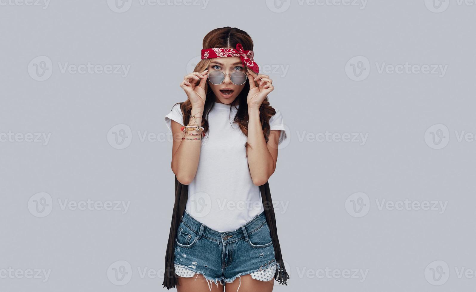 Surprised stylish young woman looking at camera and making a face while standing against grey background photo