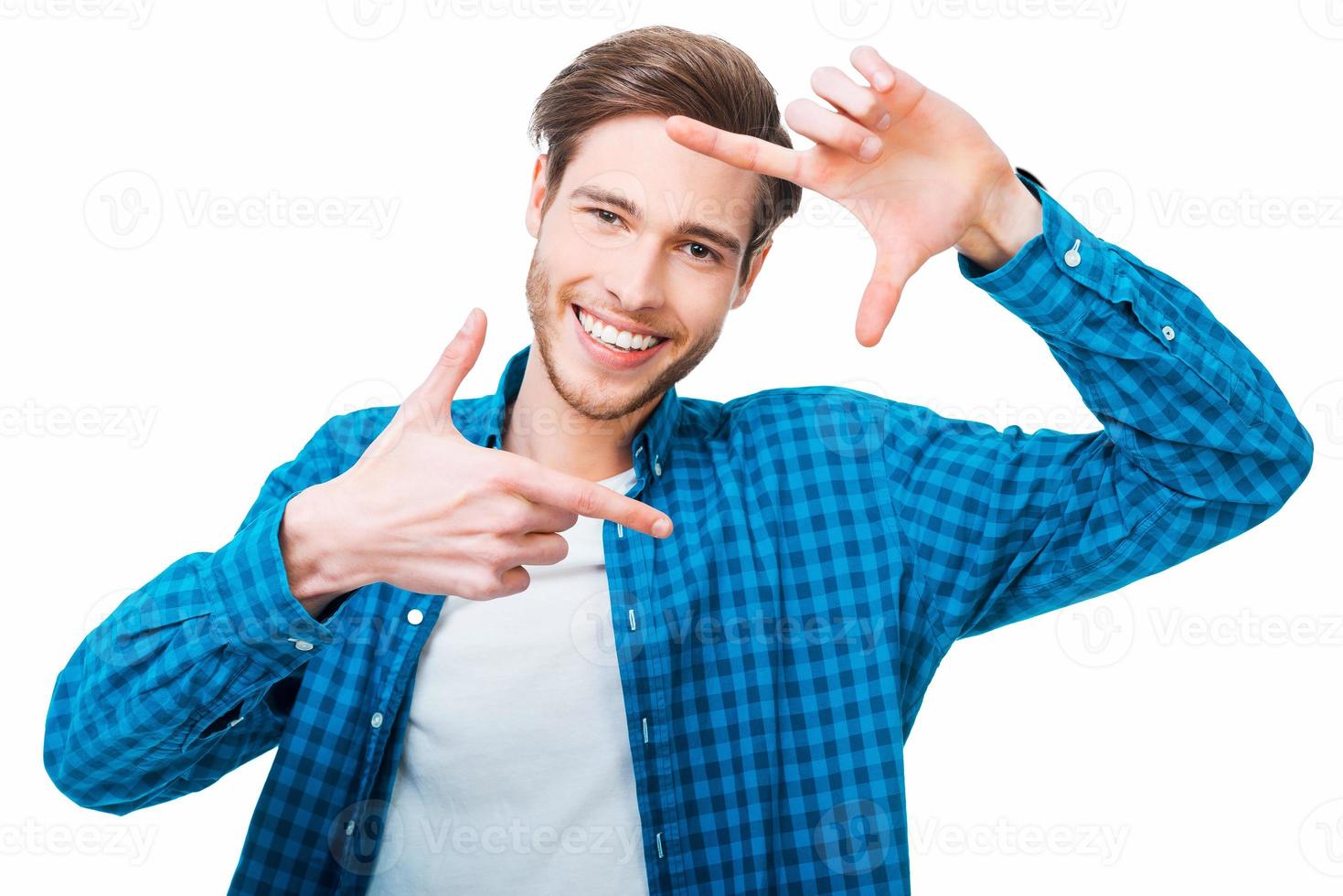 Finger frame. Handsome young man gesturing a finger frame and looking at camera while standing against white background photo