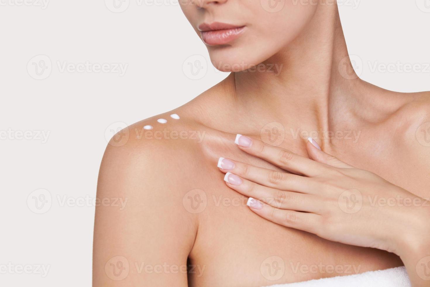 Skin care. Part of beautiful young woman with cream on her shoulder standing against grey background photo