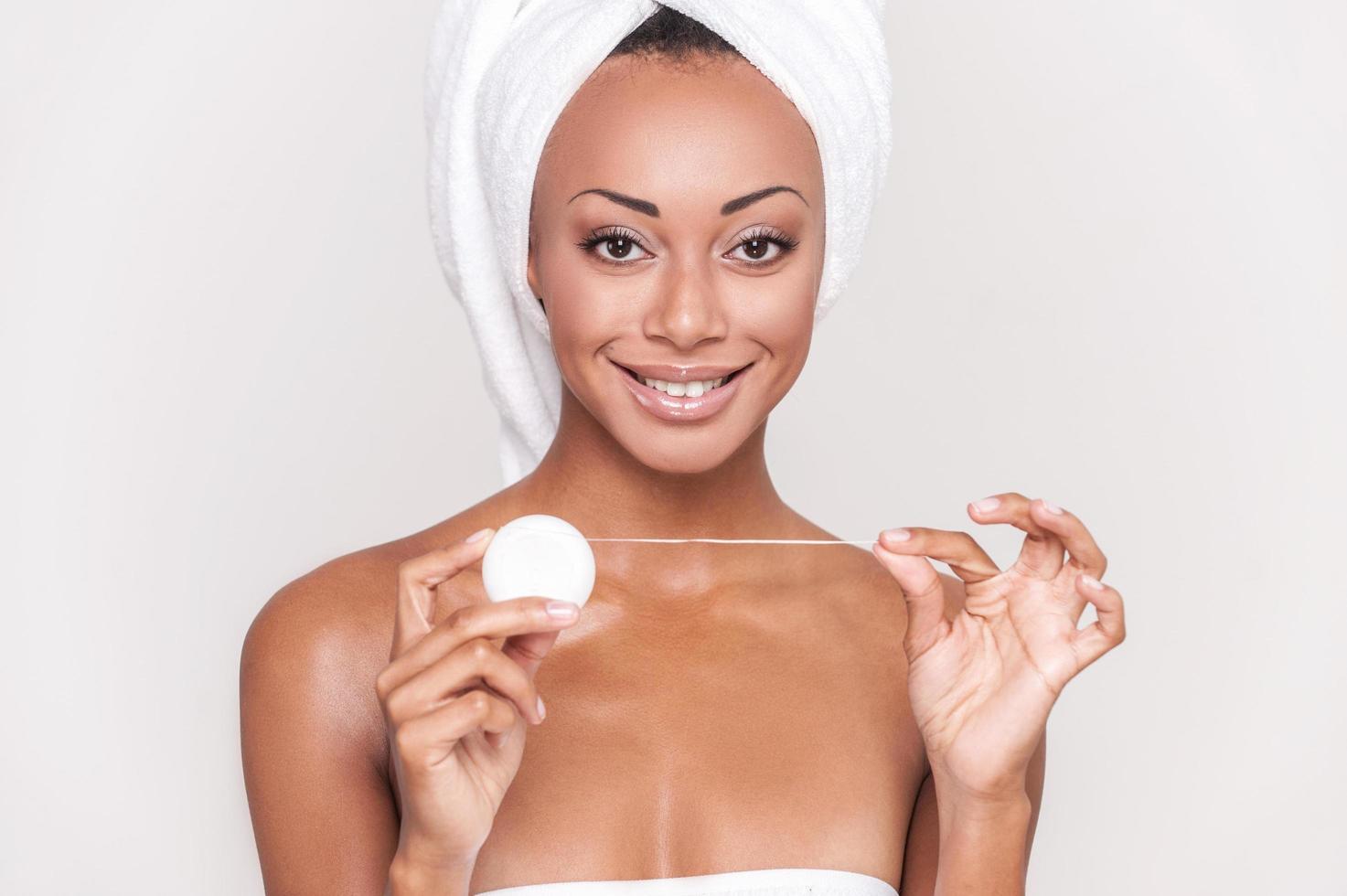 Dental cleaning. Beautiful young Afro-American woman holding dental floss and smiling at camera while Isolated on gray background photo