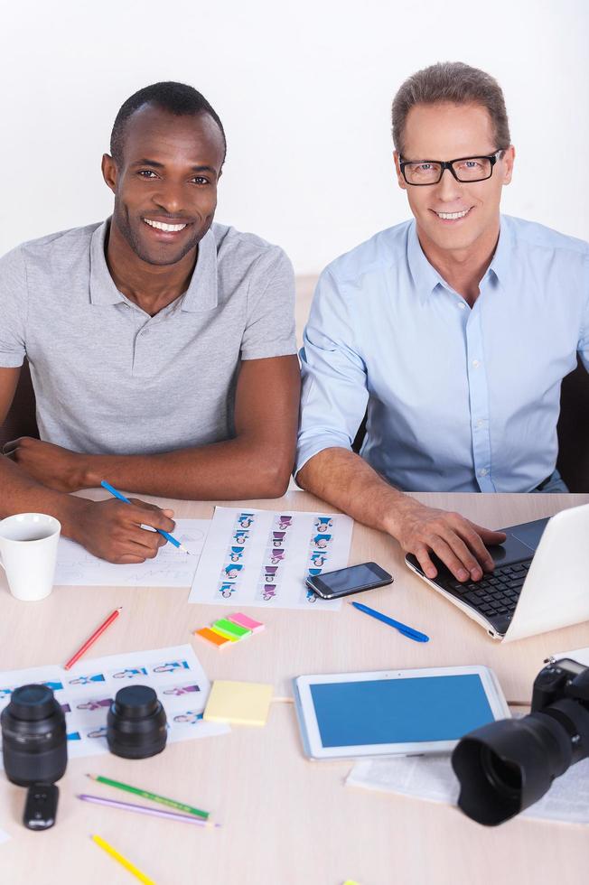 compañeros de trabajo creativos en el trabajo. vista superior de dos empresarios alegres con ropa informal sentados juntos en la mesa y mirando la cámara foto