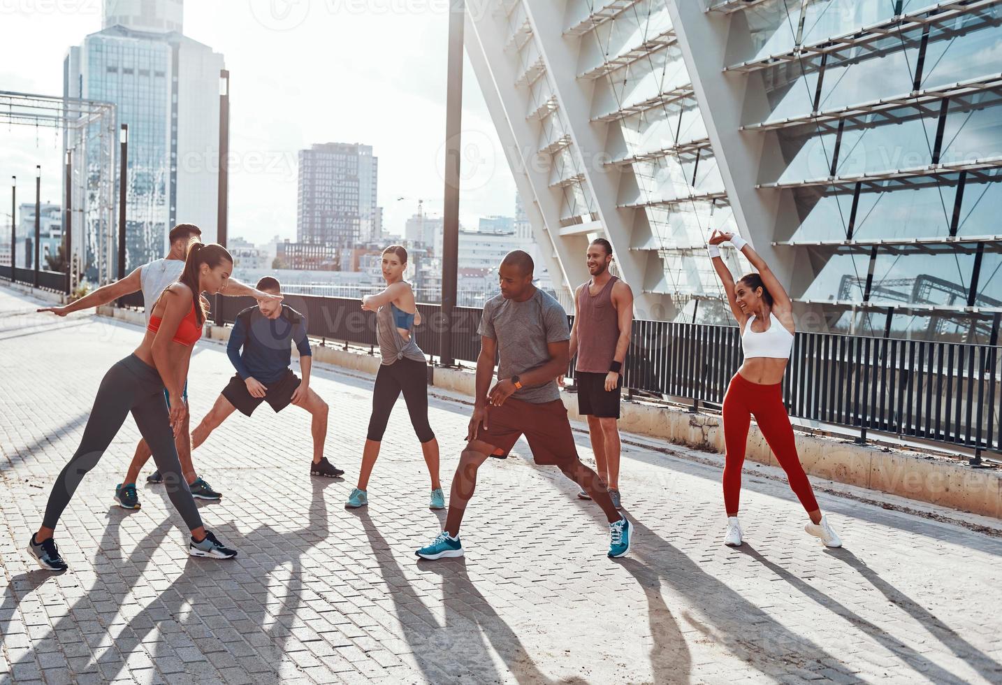 Full length of people in sports clothing warming up and stretching while exercising outdoors photo