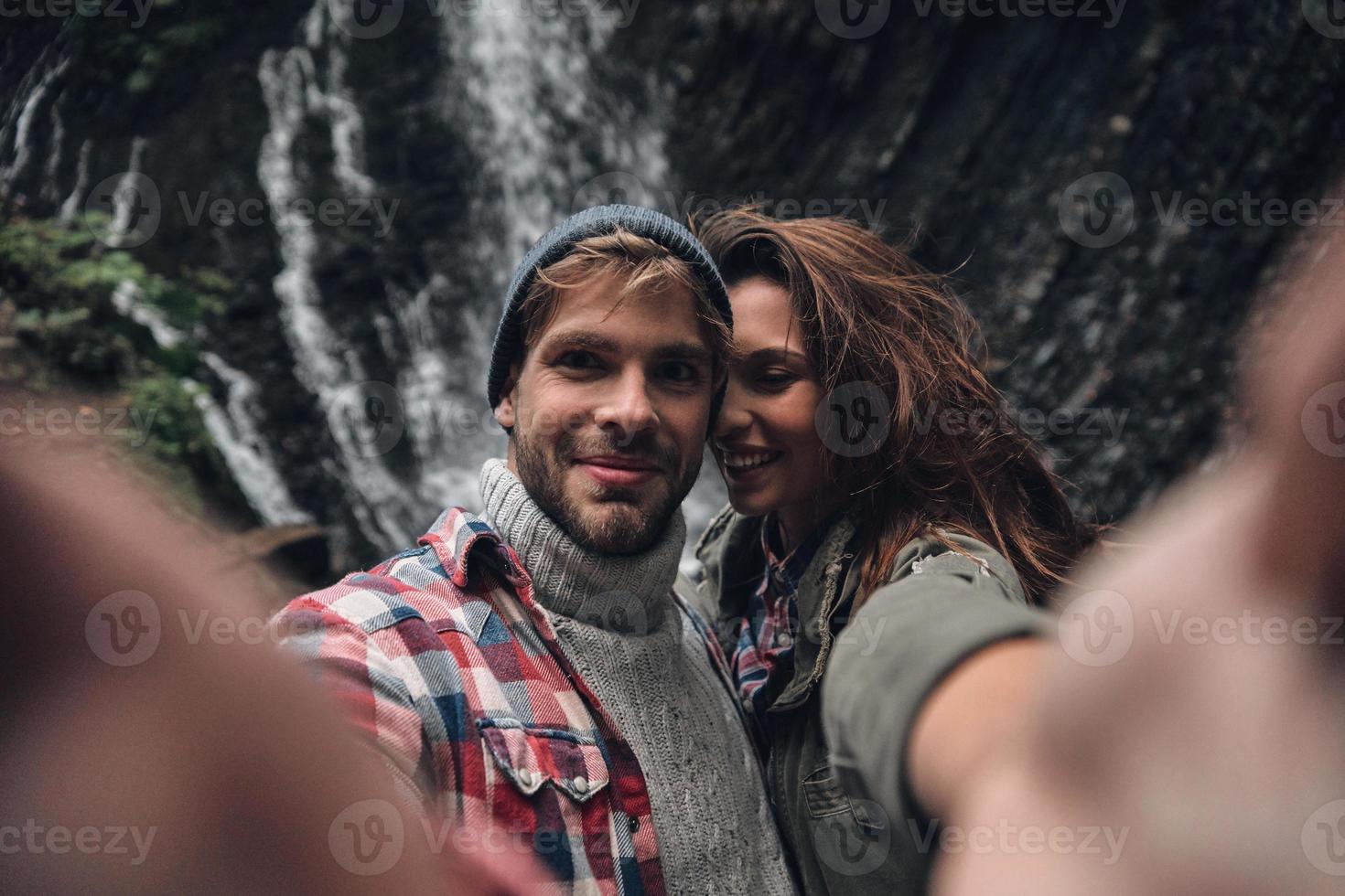 Self portrait of beautiful young couple smiling while standing outdoors with the waterfall in the background photo