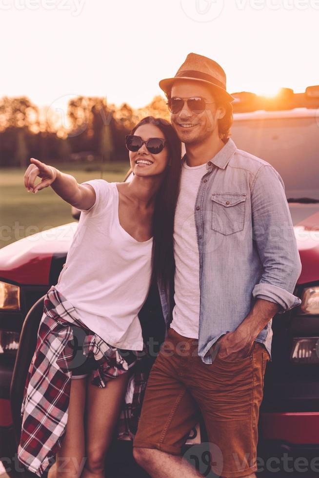 Look over there Beautiful young couple bonding to each other and leaning at their pick-up truck while woman pointing away and smiling photo