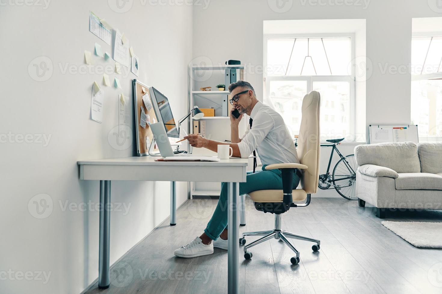 Ready to do business. Good looking young man talking on the phone while sitting in the office photo