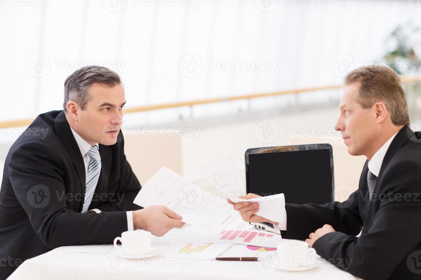 Business confrontation. Two mature men in formalwear arguing while sitting together at the table photo