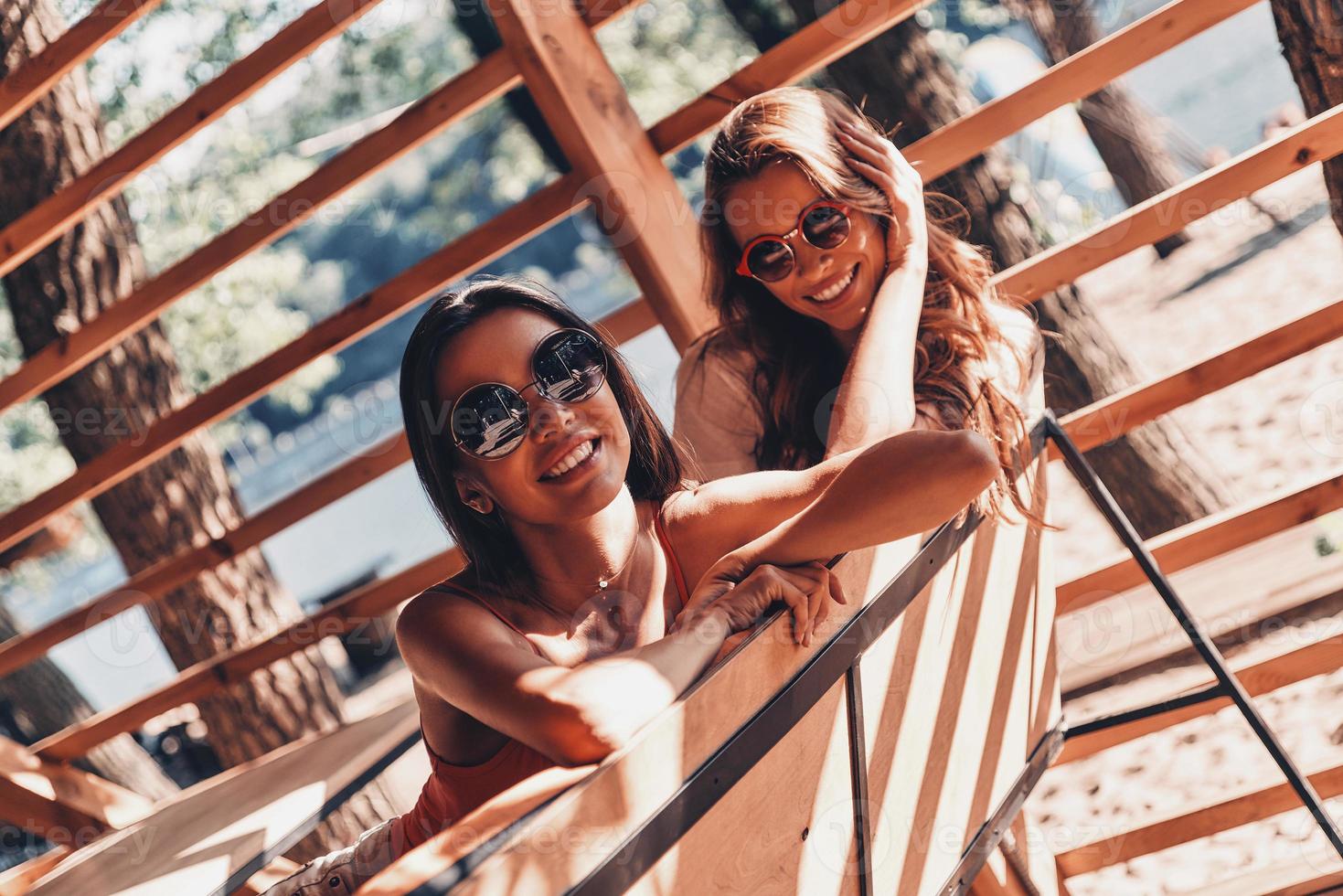 Summer makes them happy. Two attractive young women smiling while sitting in the beach cafe photo