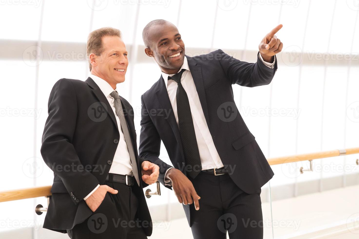 Business people. Two cheerful business men standing close to each other while one of them pointing away and smiling photo