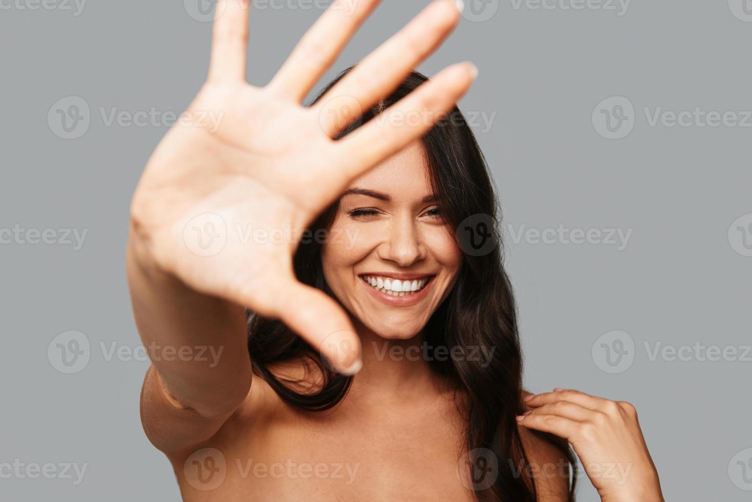 Feeling playful. Beautiful young woman winking and gesturing while standing against grey background photo