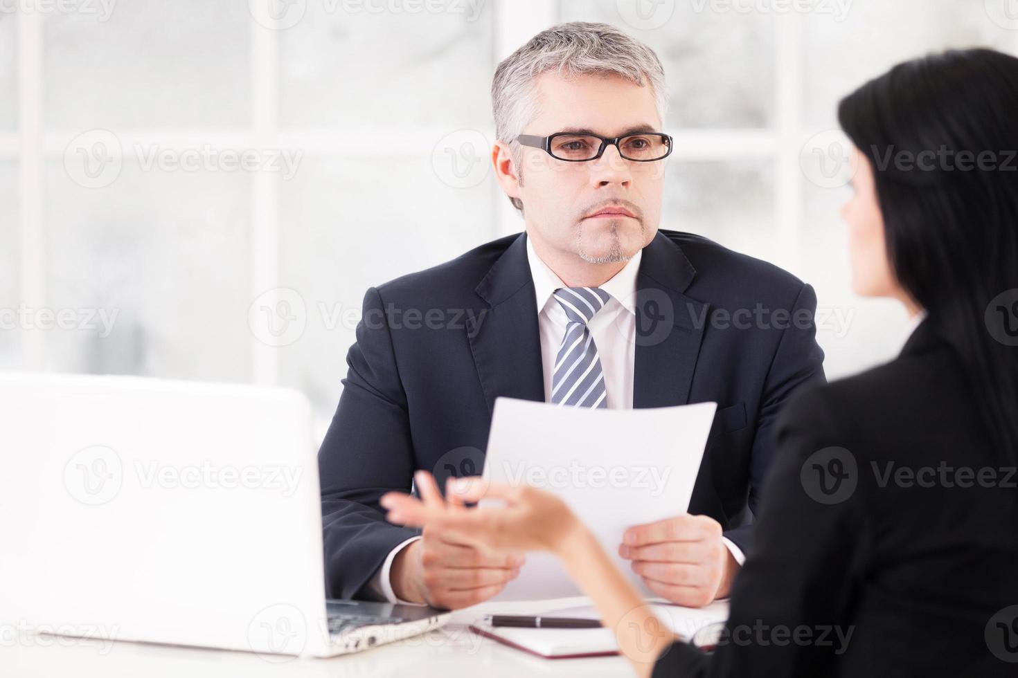 Job interview. Confident senior man in formalwear sitting at the table while woman in suit sitting in front of him and gesturing photo