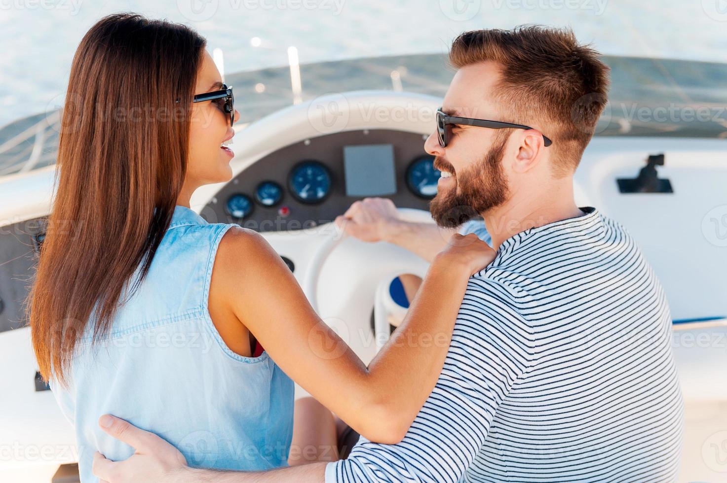 Their love is bigger than ocean. Happy young couple looking at each other and smiling while driving yacht photo