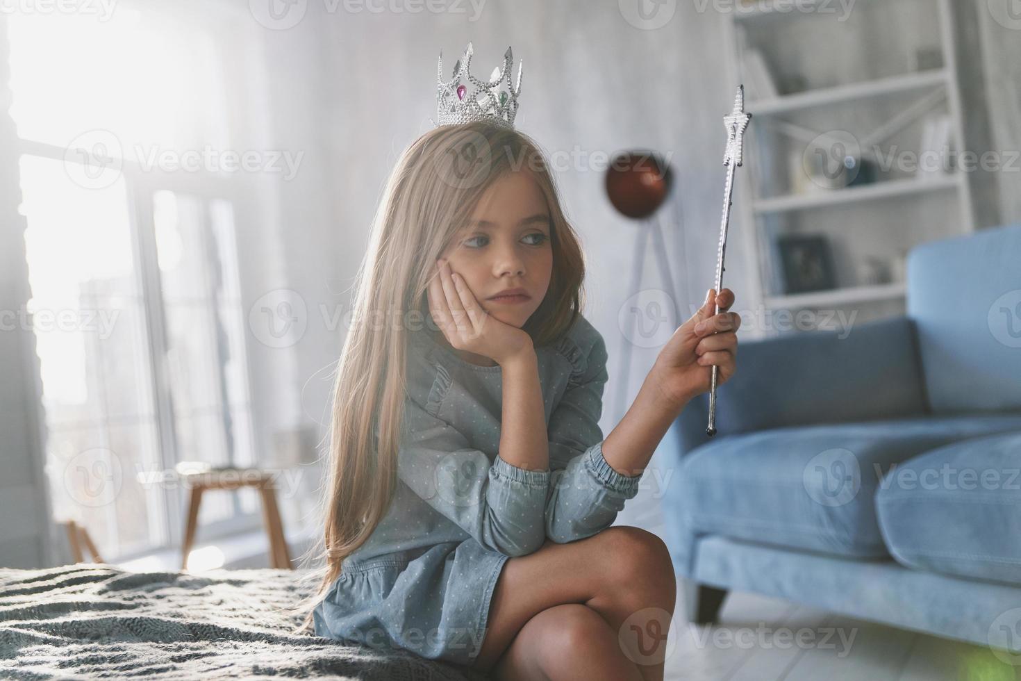 Spell does not work. Disappointed little girl playing with a magic wand and looking away while spending time at home photo