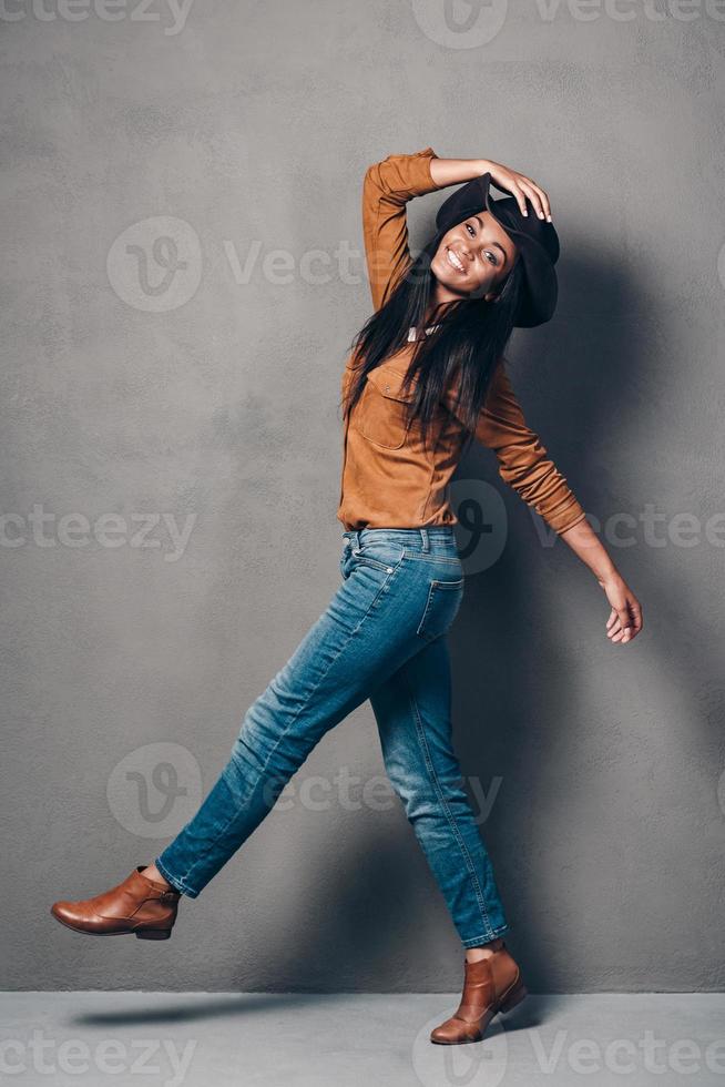 Pure joy and style. Full length of beautiful young African woman in hat posing and looking at camera with smile while standing against grey background photo