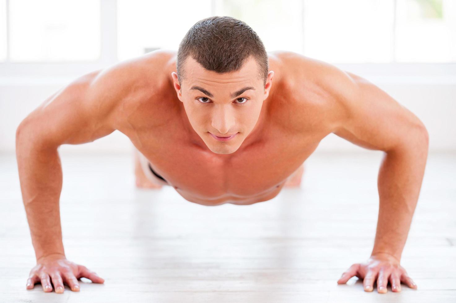 Man doing push-ups. Young muscular man doing push-ups and looking at camera photo