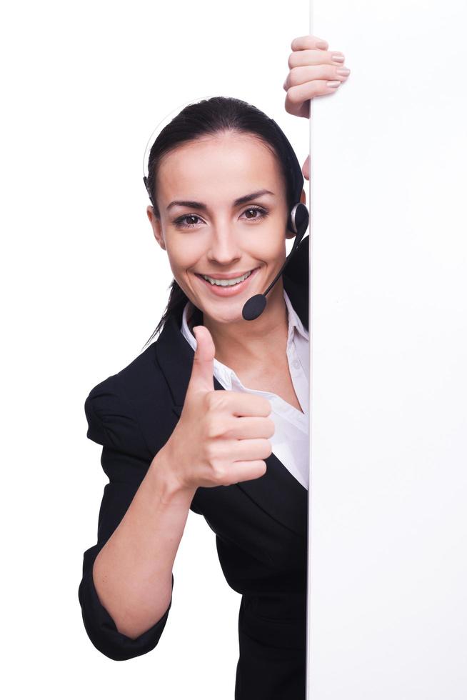 Providing only quality support. Beautiful young woman in headset standing near copy space and smiling while isolated on white photo