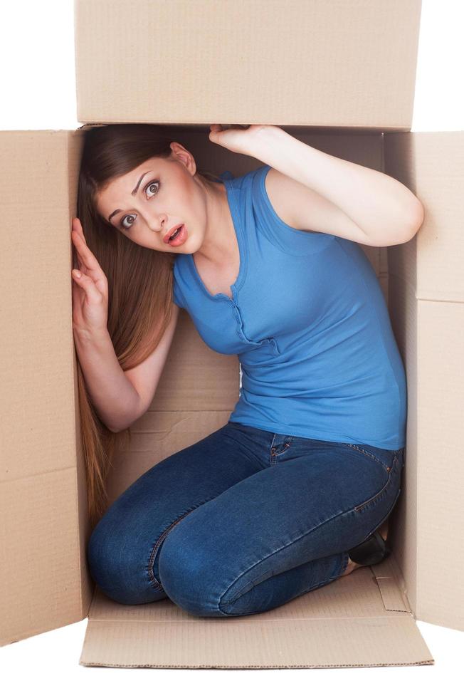Trapped inside. Shocked young woman looking at camera while sitting in a cardboard box photo