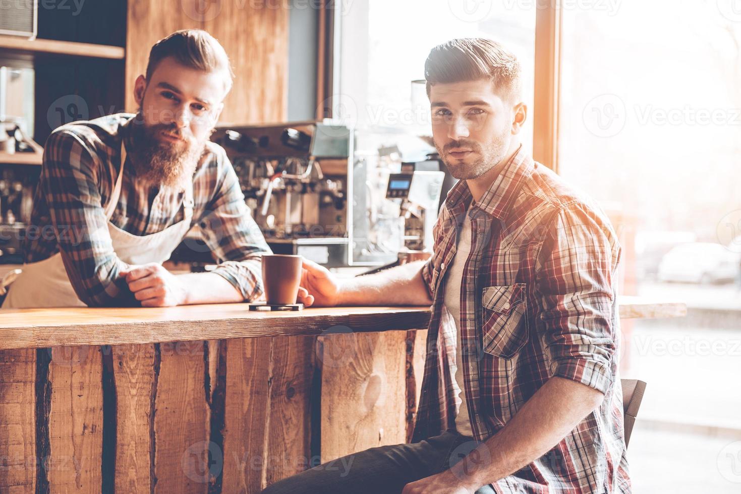 Spending great time at coffee shop. Two handsome men looking at camera while sitting at bar counter at cafe photo