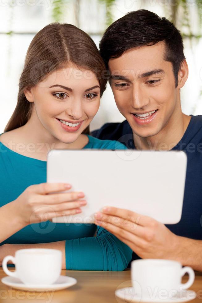 Living at the digital age. Cheerful young loving couple sitting at the restaurant and using digital tablet photo