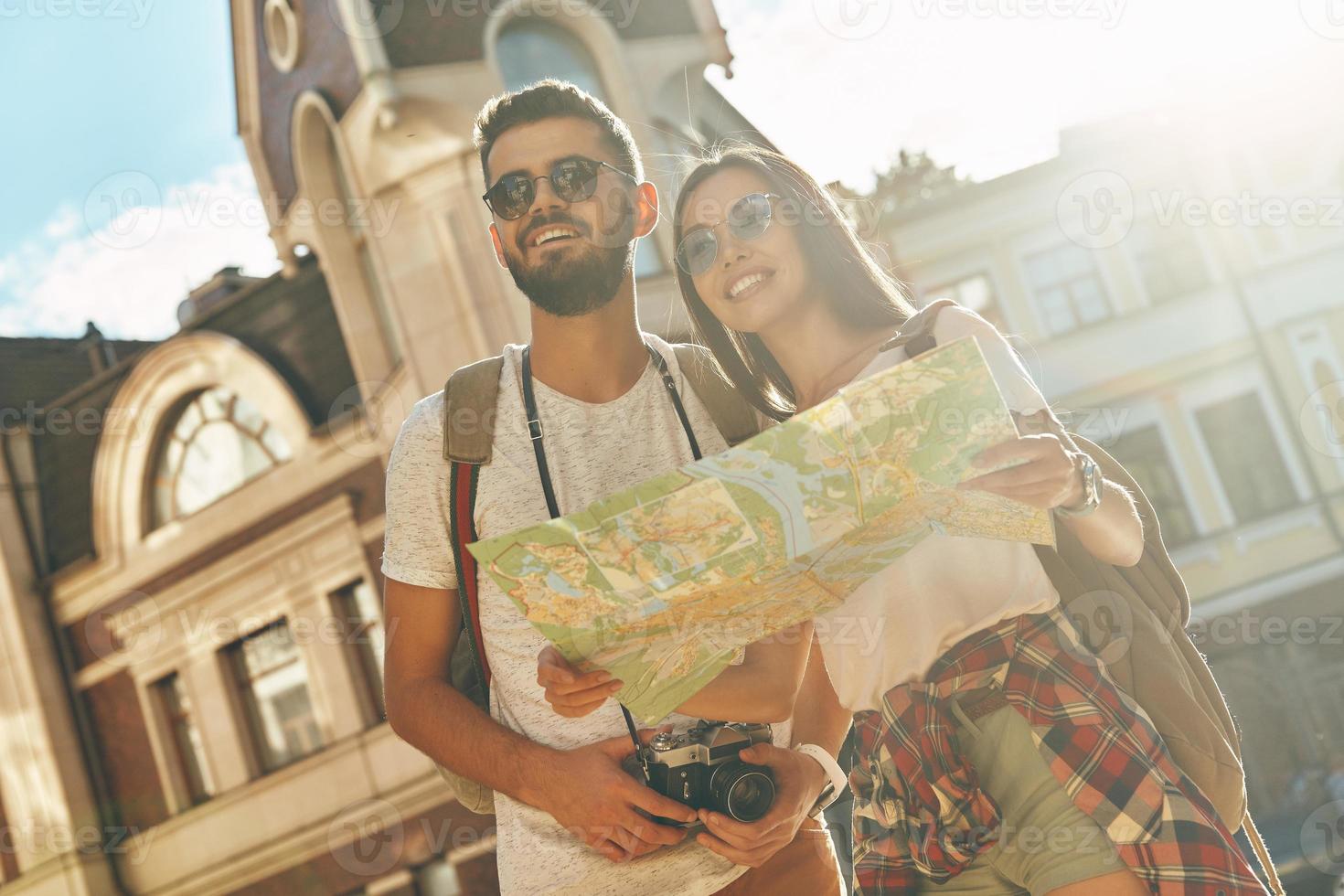 Beautiful young couple holding map and smiling while standing outdoors photo