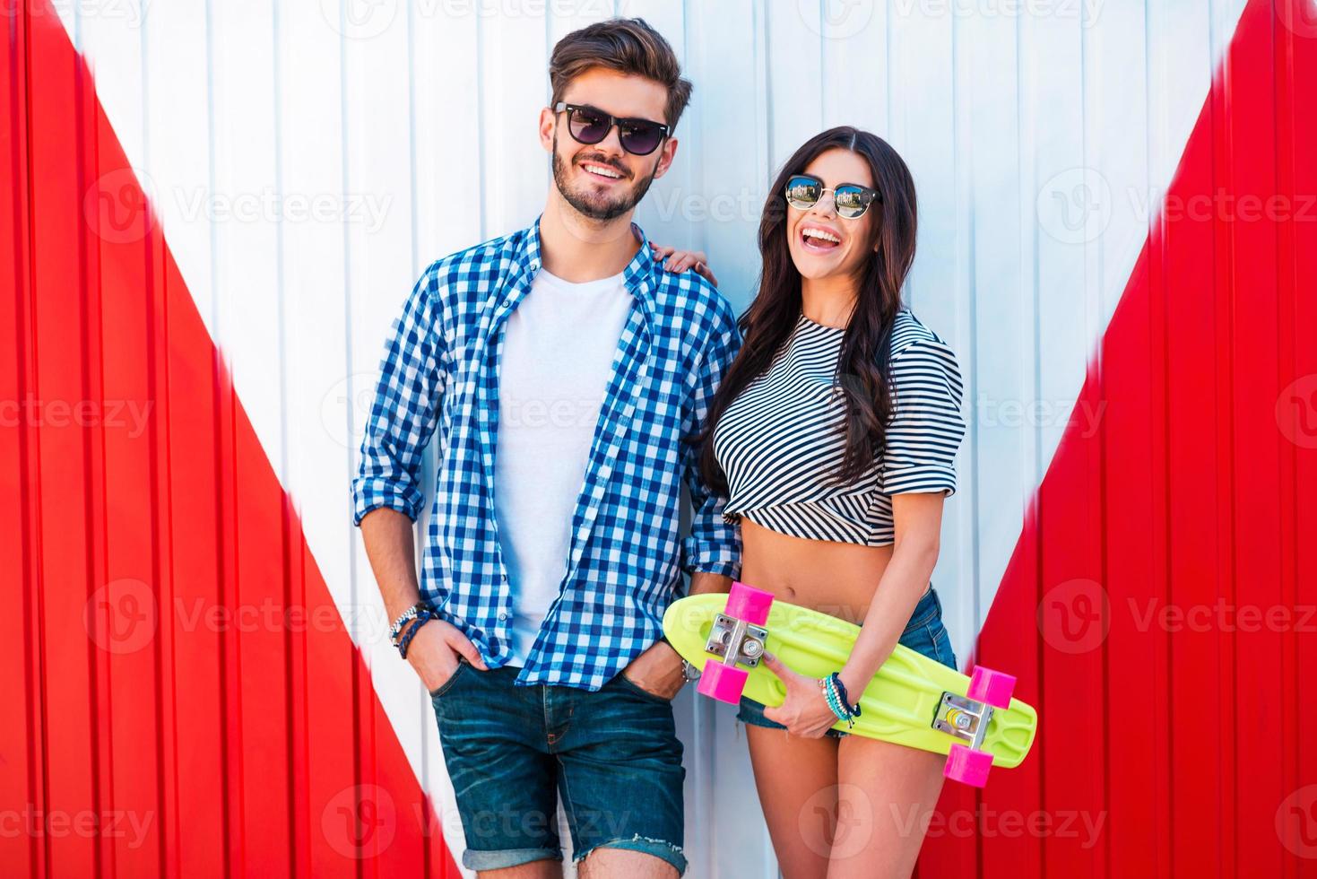 Funky couple. Cheerful young woman holding skateboard and bonding to her boyfriend while standing outdoors photo