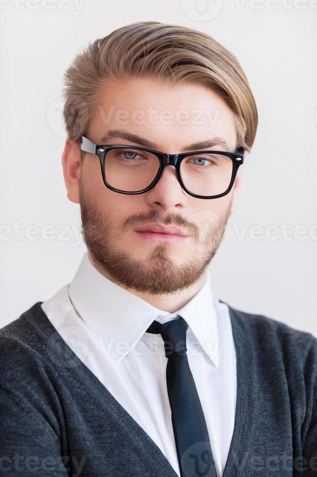 Portrait of confidence. Portrait of handsome young man in glasses looking at camera while standing against grey background photo