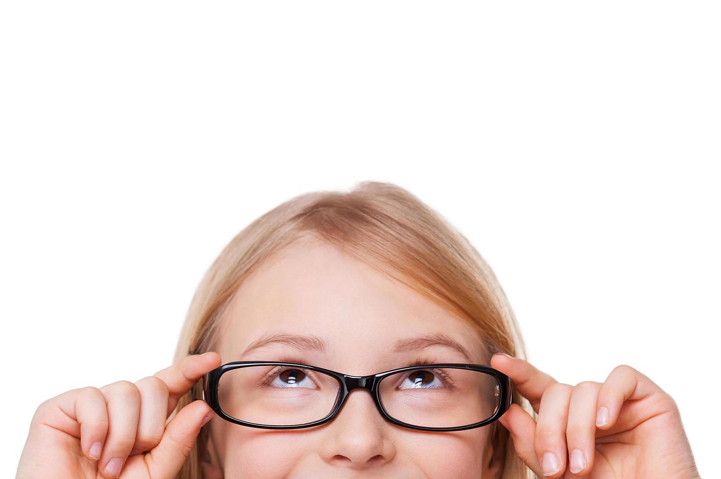 Curious little girl. Cropped image of cheerful little girl adjusting her glasses and looking up while isolated on white photo