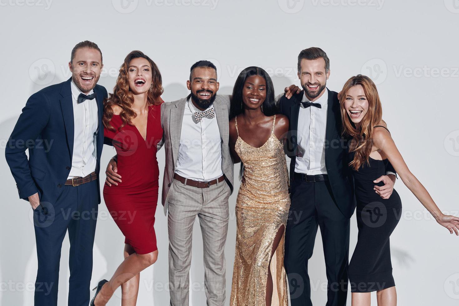 Group of beautiful people in formalwear bonding and smiling while standing against gray background photo