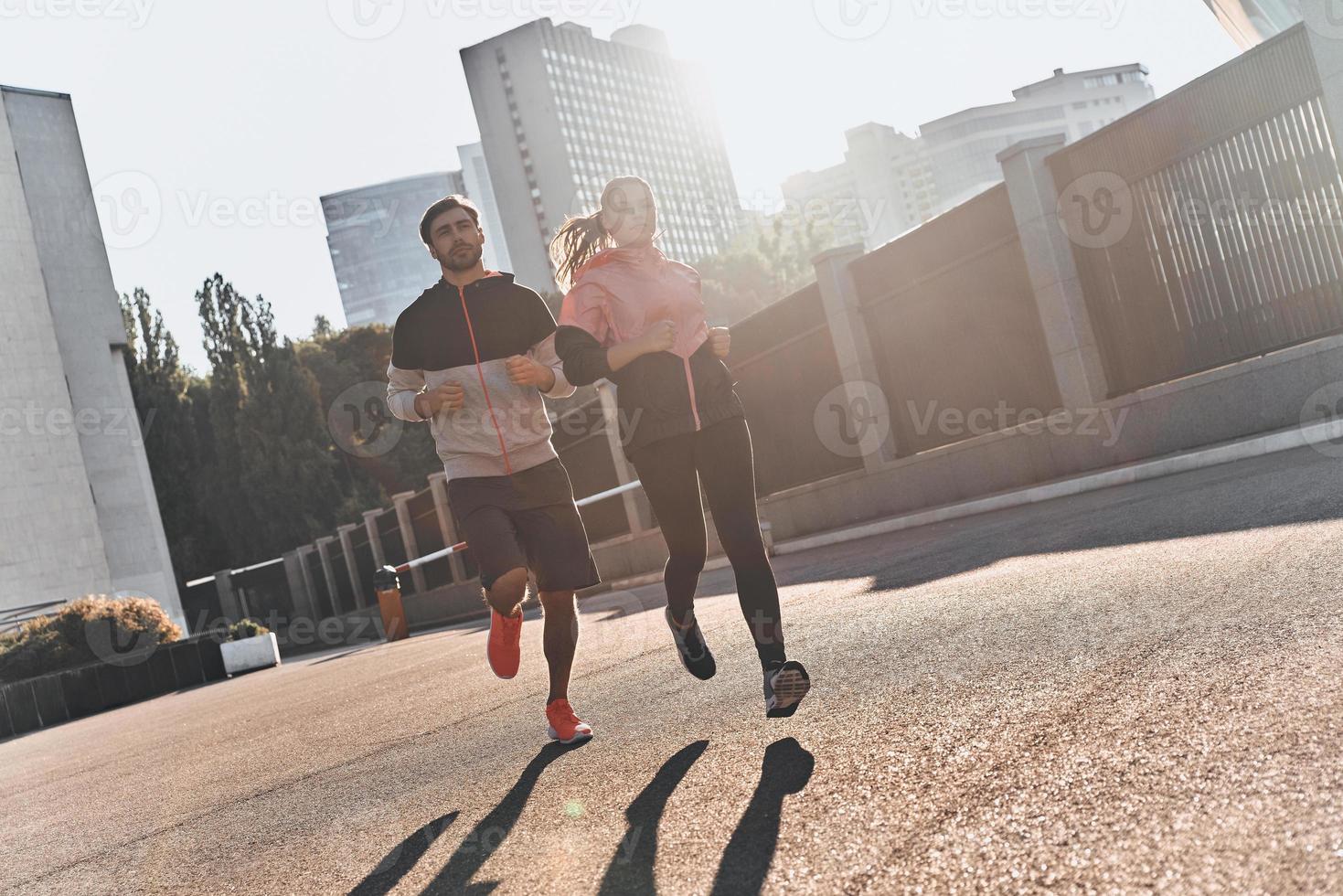 Best jog ever. Full length of young couple in sport clothing running through the city street together photo
