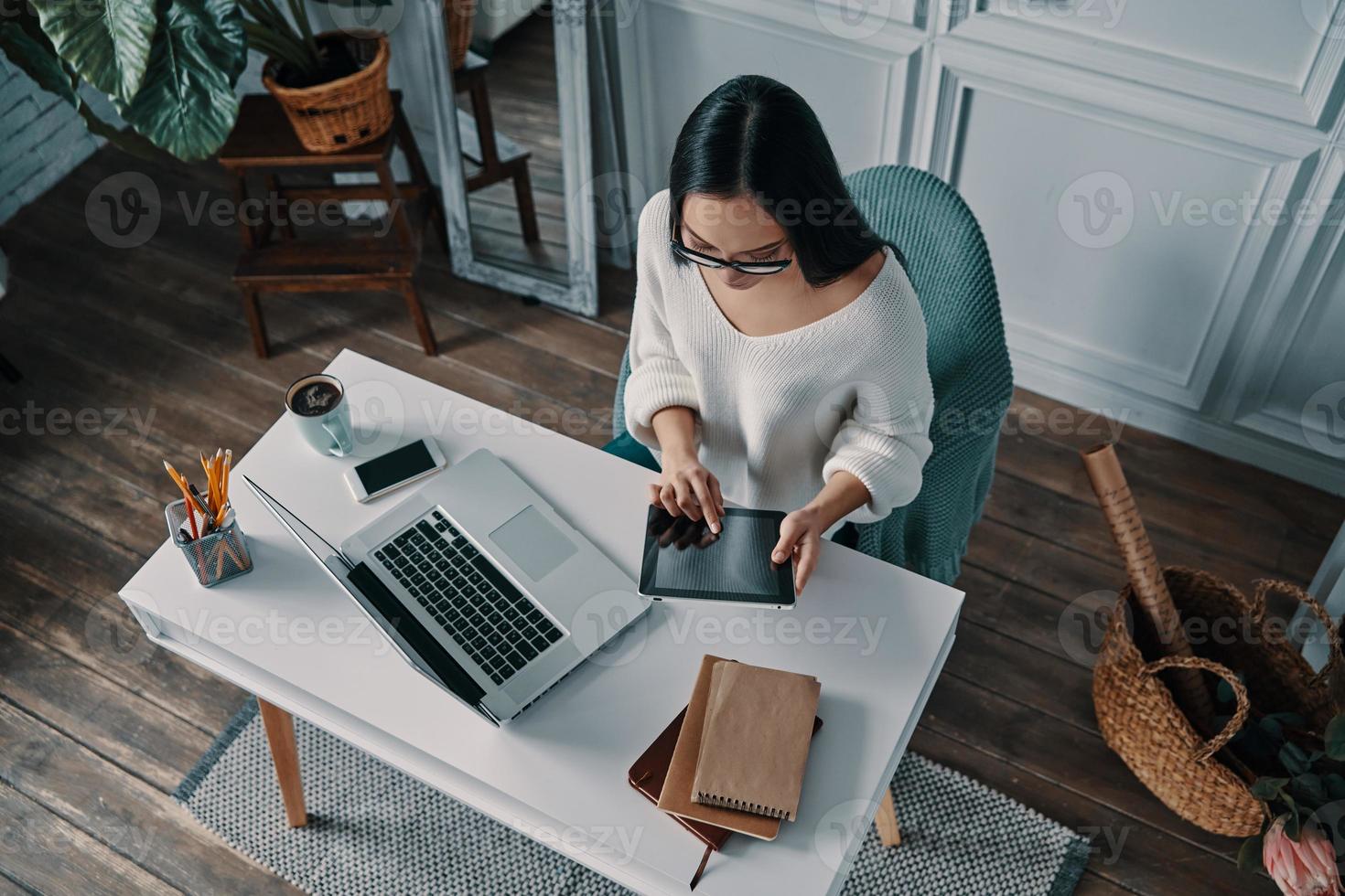 Another deadline. Top view of beautiful young woman working using digital tablet while sitting in home office photo