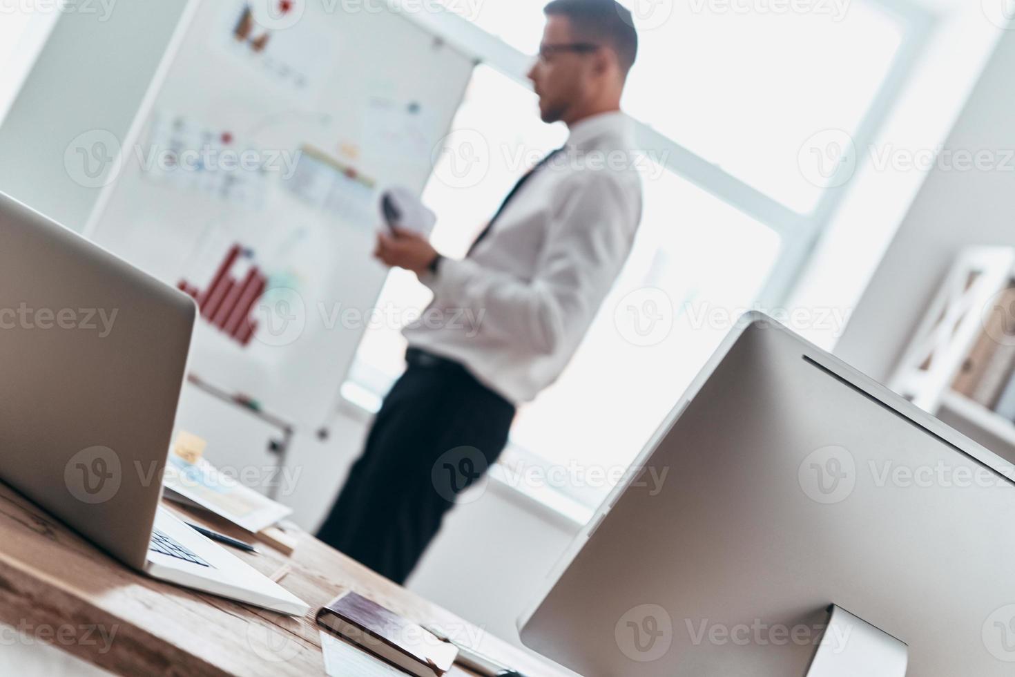 Paying attention to every detail. Busy young man in formalwear working with information on the graph while standing in the office photo