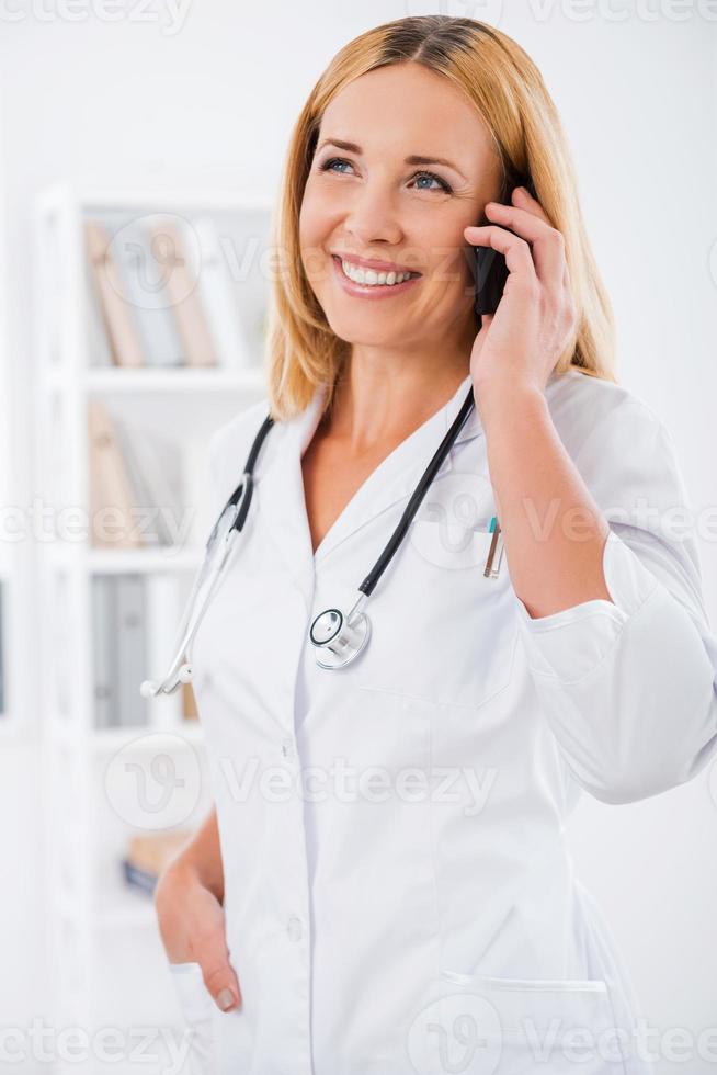 Good news for her patient. Happy female doctor in white uniform talking on the mobile phone and smiling photo