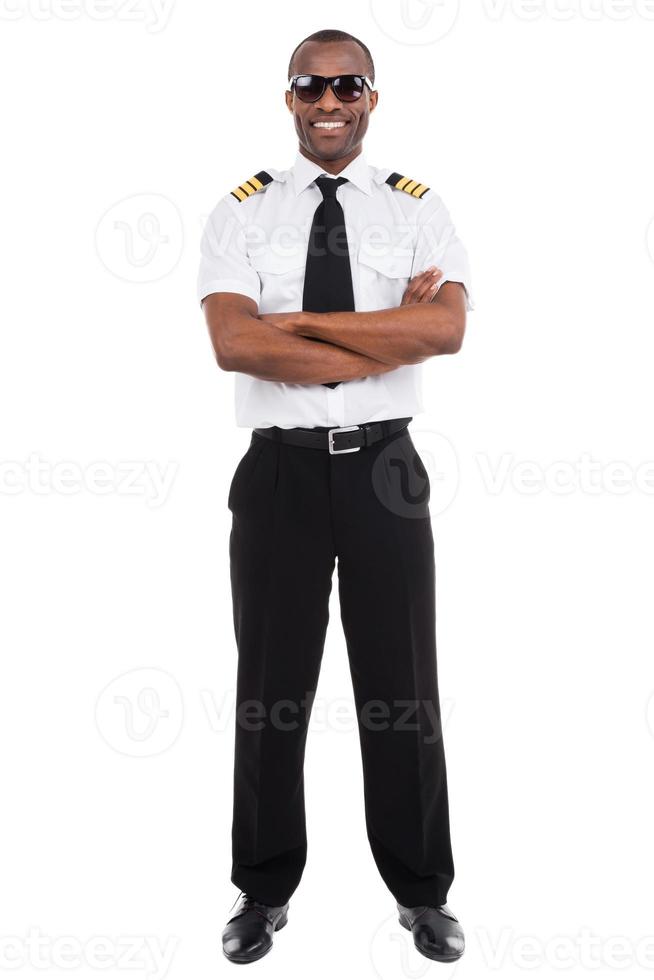 Confident pilot. Full length of confident male pilot in uniform keeping arms crossed and smiling while standing against white background photo