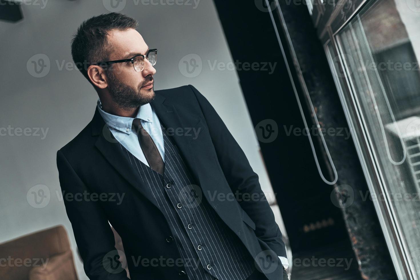 Thinking about... Thoughtful man in full suit looking away through the window while standing indoors photo