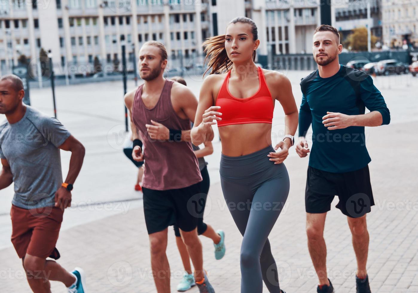 Group of young people in sports clothing jogging while exercising on the sidewalk outdoors photo