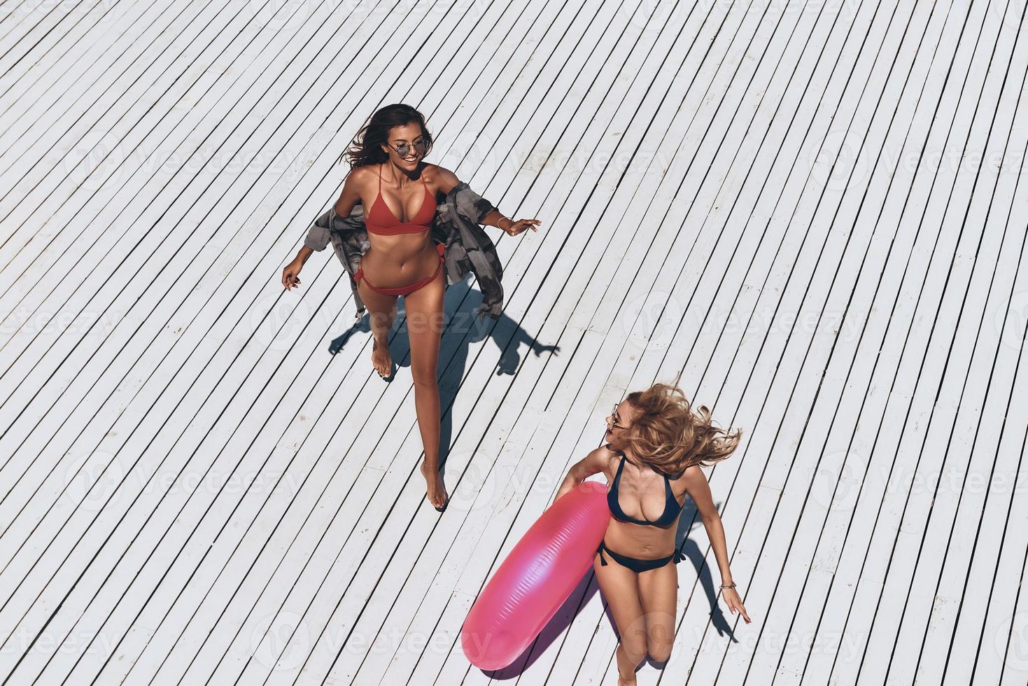 Fun under the sun. Top view of two beautiful young women in bikini smiling while running outdoors photo