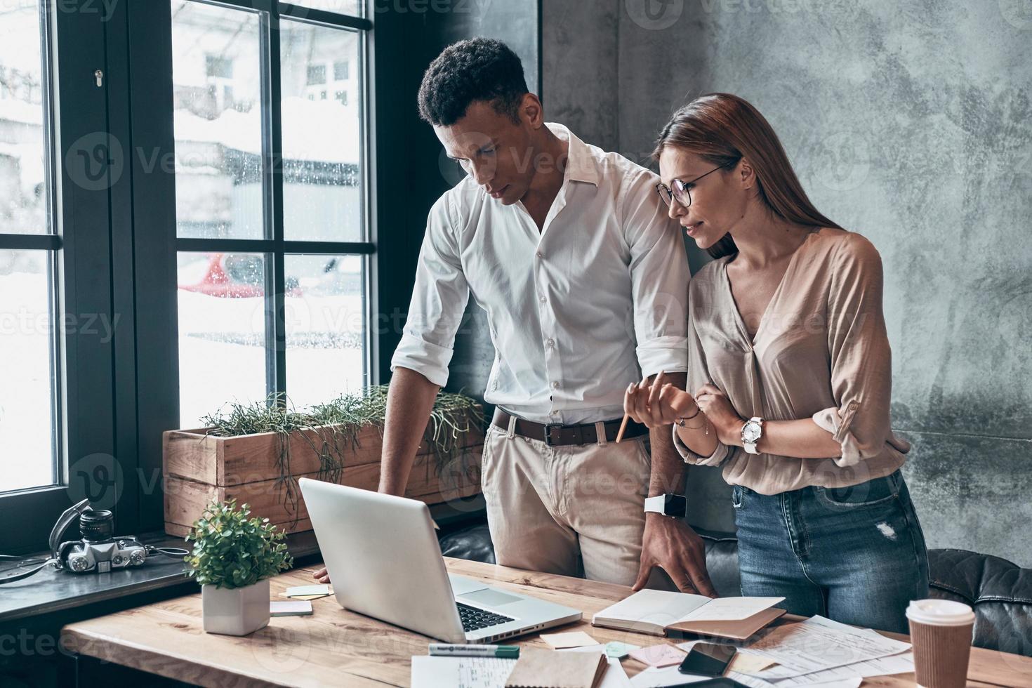 Two young coworkers in smart casual wear discussing business while working in office together photo