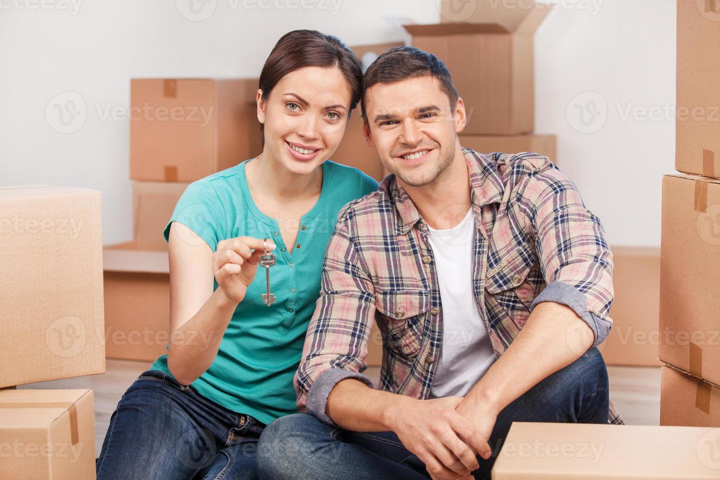 Key of their new apartment. Cheerful young couple sitting close to each other and smiling while holding key from the house photo