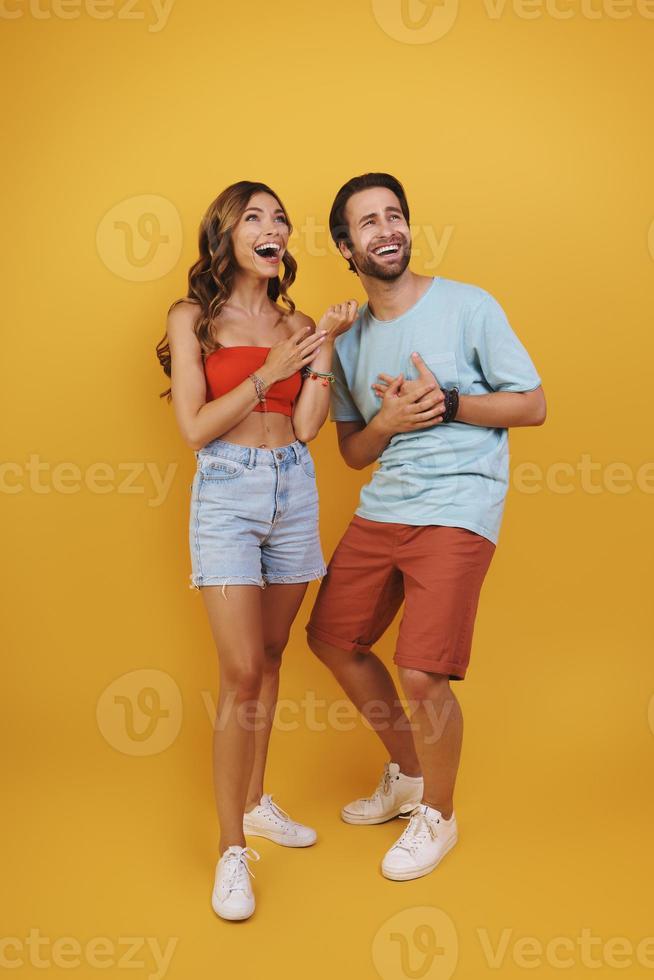 Full length of beautiful young couple smiling and looking away while standing against yellow background photo