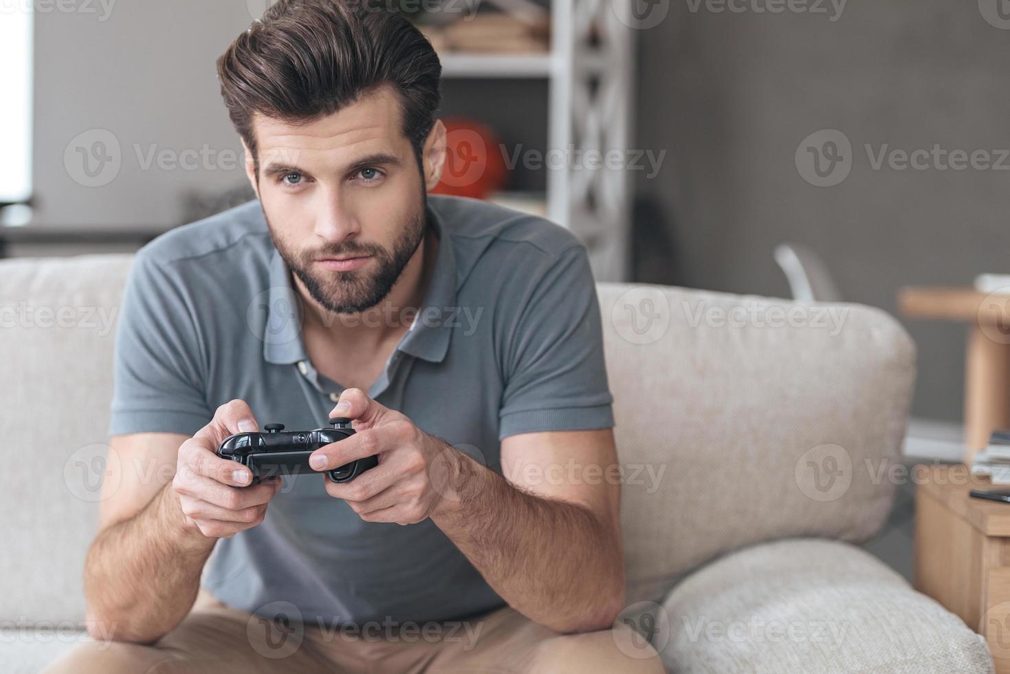 Totally concentrated on his game. Handsome young man playing video game while sitting on the couch at home photo