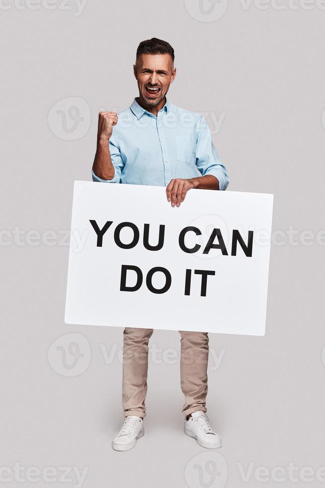Believe in yourself Full length of handsome young man holding poster and gesturing while standing against grey background photo
