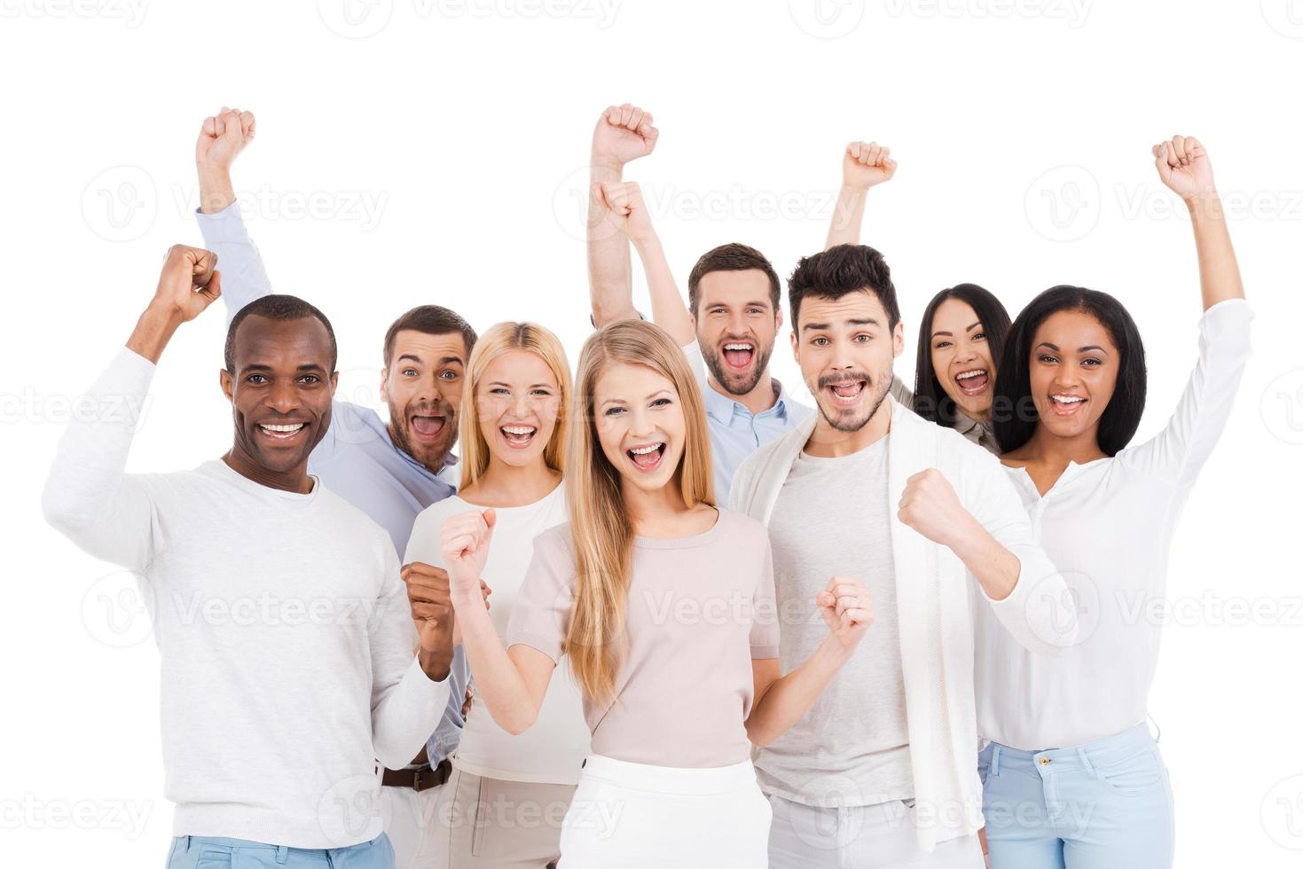 Successful team. Group of happy young people in smart casual wear looking at camera and keeping arms raised while standing against white background photo