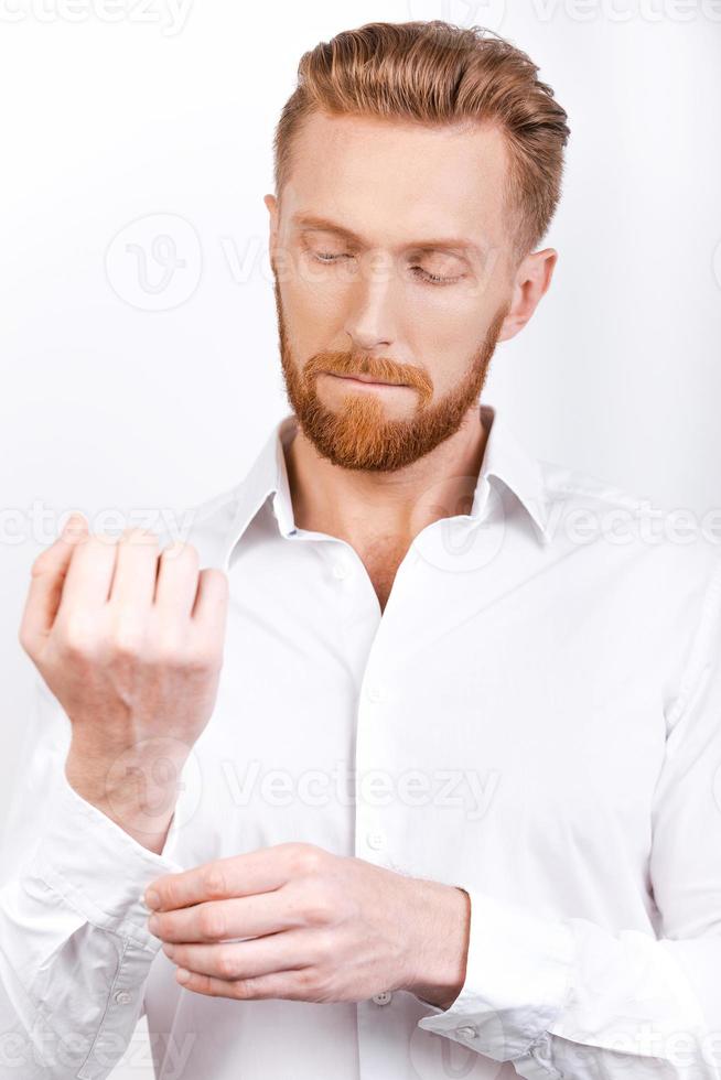 Everything should be perfect. Confident young bearded man adjusting sleeves while standing against white background photo