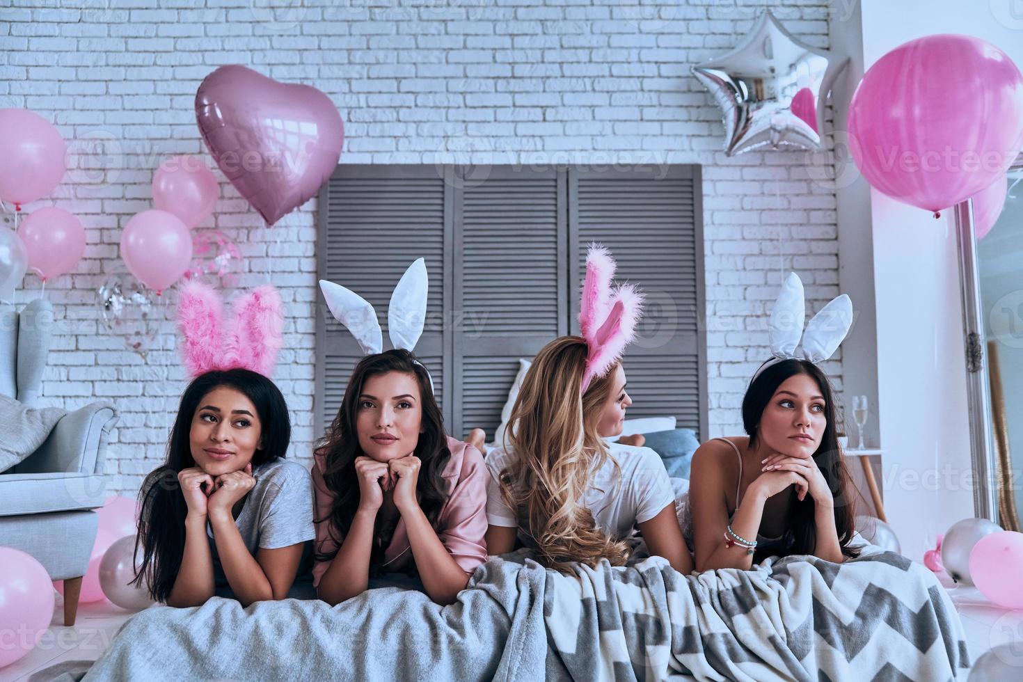 Feeling uncertain. Four beautiful young women in bunny ears looking away while lying on the bed photo