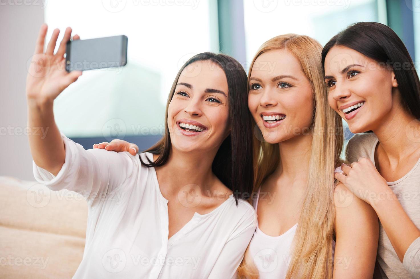 Fun in focus. Three beautiful young women making selfie and smiling while sitting on the couch together photo