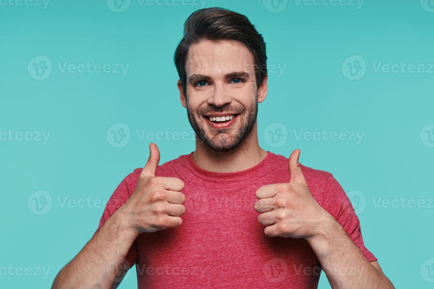 Handsome young man in casual clothing looking at camera and showing his thumbs up photo