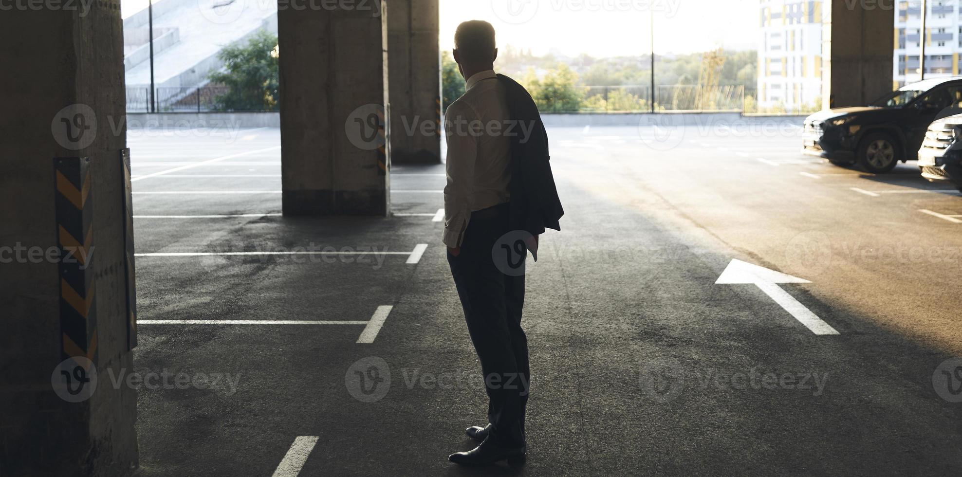 Rear view of mature man in formalwear standing on parking lot photo